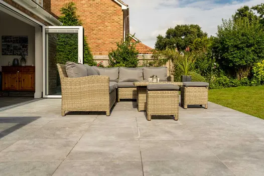 Silver Contro porcelain patio with large rattan outdoor lounge set. Its mid-brown cushions tone with the 600x600mm paving slabs.