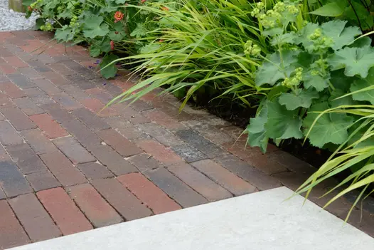 Section of Abbey Dark clay pavers laid between gravel and pale paving slab, next to lushly planted border. Design by Nic Howard.
