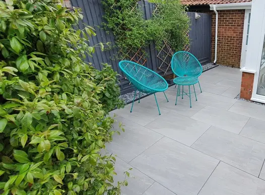 Kandla Grey Porcelain paving, with turquoise wire chairs and table against fence with trellis, designed by Absolute Landscapes.