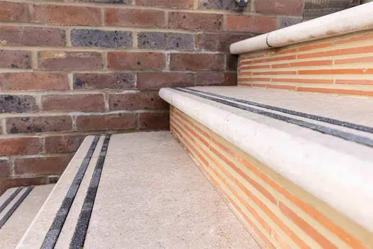 Close-up of Acid Egyptian Limestone Bullnose Step with contrasting inset safety strips against a red brick riser.