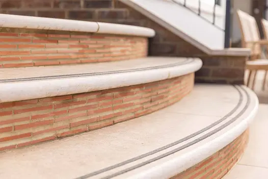 Detail of curved Acid Egyptian Limestone Bullnose Steps with grip strips, set against brick risers on garden terrace.