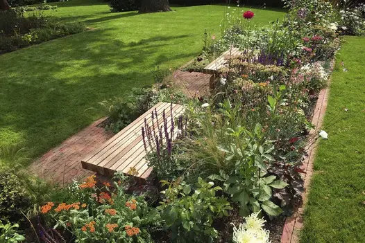 Large irregular lawn with rectangular area edged with bricks, enclosing flower beds, benches and Seville clay paving.