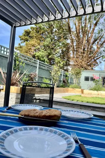 Alfresco view with plates set on blue table cloth under the proteus grey aluminium pergola with the louvres open.