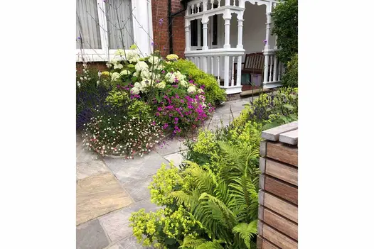 Front garden of Edwardian terraced house with Tumbled Black sandstone paving slabs leading between planted beds to wooden porch.