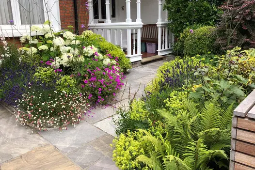 Edwardian house with black sandstone tumbled garden paving slabs leading to porch between planted borders. 