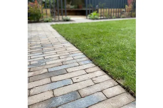 Path of grey and red Aldridge Clay Brick Paving runs down side and around corner of lawn to area fenced with palings.