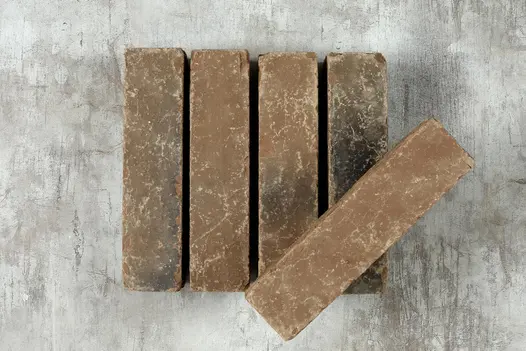 5 Aldridge clay pavers on white background, one brick placed on top of the others, showcasing their natural texture and earthy hues.