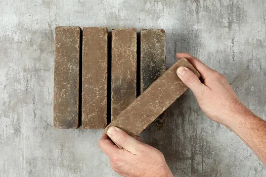 Hand displays 1 of 5 Aldridge clay pavers on a white background, showcasing its earthy colour and natural texture.