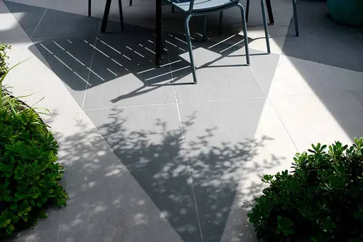 Mesmerizing shadows dance across slabs, illuminated by  gentle rays of natural sunlight, enhancing the trendy black and urban grey porcelain tiles.