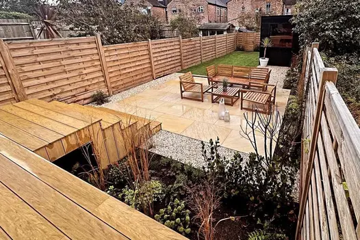 Sandstone paving and Amber DesignBoard comopsite decking seen in wet conditions, decking used as steps leads to patio.