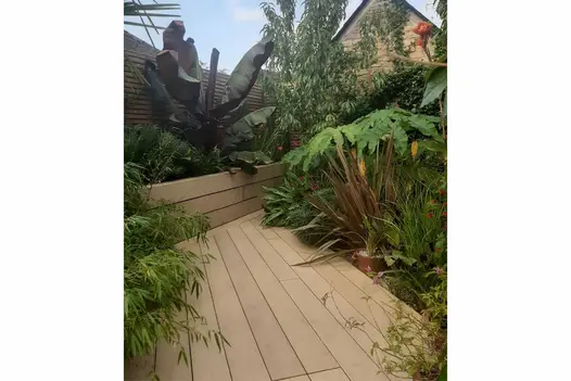 Slant-edged deck of Amber DesignBoard abuts raised bed faced with matching boards. Adjacent beds filled with exotic planting.