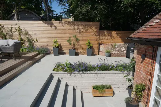 Light Grey Porcelain patio surrounded by tall timber screens and large porcelain steps leading down to patio doors.