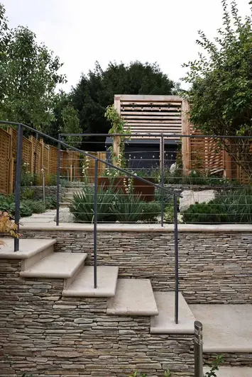 Bullnose steps adorned with cobblestone cladding leading to a verdant patio area with corten steel water feature.