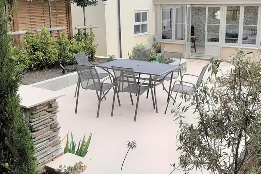 A raised patio in Florence Beige porcelain slabs, dressed with a metal furniture dining set, surrounded by raised planter beds.
