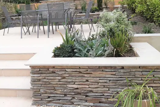 Stone clad raised wall turned planter used florence beige porcelain 5mm chamfered coping stones with matching paving on patio.