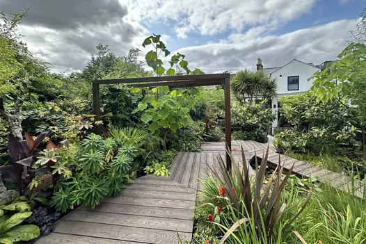 Tropical garden design featuring Millboard Antique Oak decking, surrounded by vibrant planting and architectural foliage.