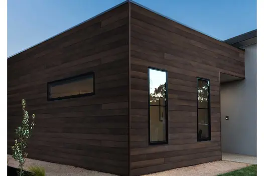 Modern building exterior clad in Antique Oak Millboard Shadow Line cladding, with deep brown finish and vertical black-framed windows.