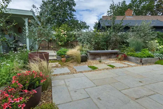 Fenced garden paved with Antique Yellow limestone slabs and gravel. Relaxed planting, shrubs in trugs and timber sleeper bed.