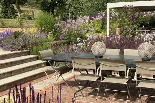 Long metal dining set sits on clay paver patio with Antique Yellow Limestone bullnose steps rising between planted beds.