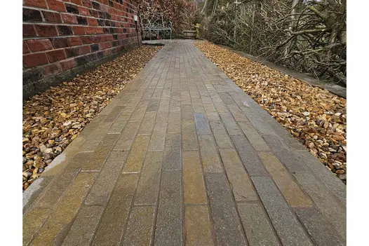 Antique Yellow Stone Pavers used as path down alleyway, the patio bricks have pebbles either side, leading to metal bench.