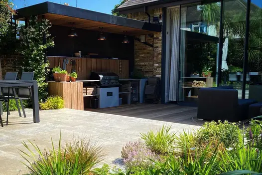 Tall glass sliding doors open onto decking and bar area, with step up to patio paved with Jura Grey smooth limestone slabs.