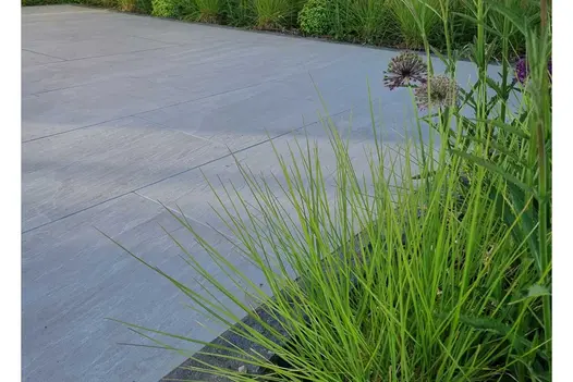 close up shot of Kandla Grey Porcelain Paving Garden Tiles UK showing the unique texture. Planting blurred in the foreground.