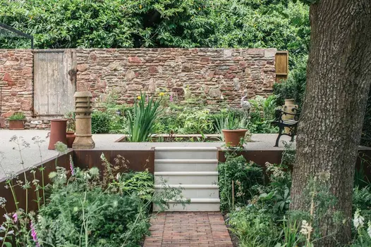 Path of Dorset Antique Clay Paver bricks lead up to sandstone steps and raised patio area with water feature.