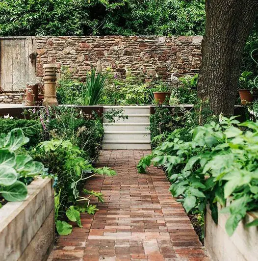 A path of Dorset Antique Clay Paver bricks leads up to sandstone steps and a raised patio area with a water feature.