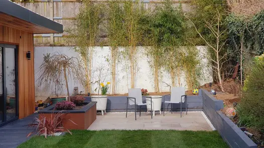 Small entertaining area at the back of the garden with painted timber flower beds and a porcelain patio looking across a lawn.