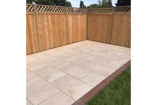 Corner of a garden with a tall closed board adjoining fence panels and a Porcelain patio edged with a red concrete block paver.