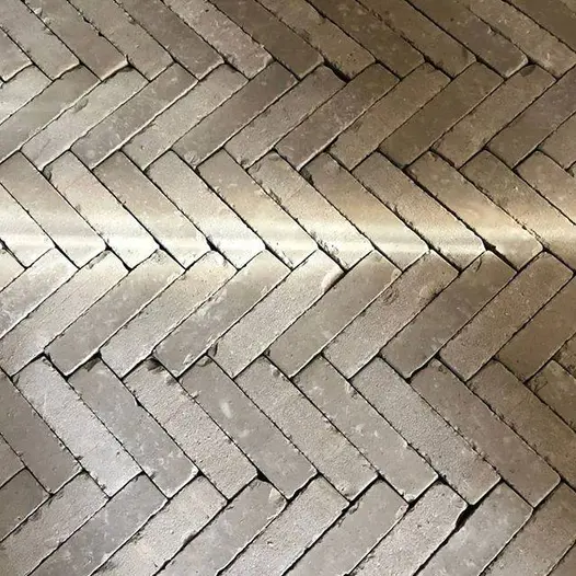 View from above of stone grey brick paving laid in herring bone pattern with shaft of light across surface. Laid by Atelier West.