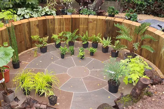 Autumn Brown Sandstone Circle edged by planting, with sinuous path leading to large wooden garden room. By No.30 Design Studio.