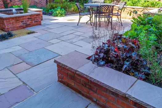 Shady view shows raised flowerbeds topped with autumn brown Indian sandstone rock-faced coping stones.