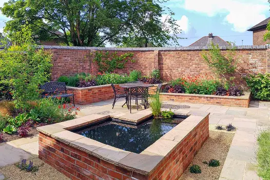 Raised L shaped pond sits in the middle of autumn brown patio, topped with matching indian rock-faced coping stones.
