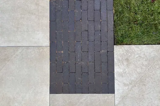 Overhead picture of an Ash Beige porcelain paving patio with a contrasting strip of dark grey clay pavers adjoining a new lawn.