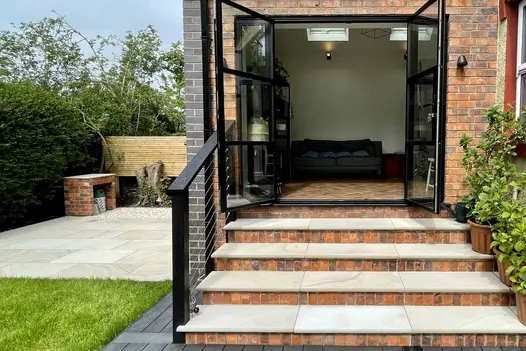 4 Light Buff sawn sandstone bullnose steps with brick risers and metal railing ascend to open double doors at rear of house.