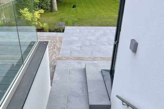 By side of house, view from above onto patio of Florence Storm outdoor tiles, with clay paver detailing. Built by Bark Brick Block.