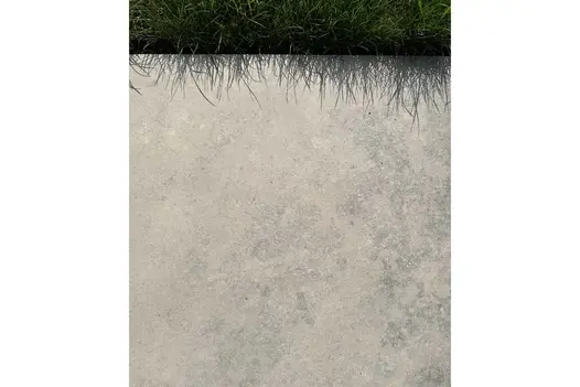 Jura Grey Porcelain paving slab laid up against a lawn with the shadows of the grass dappling over the edge of the paving.