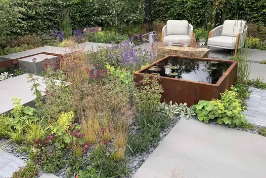 Steel corten water feature and two outdoor armchair sit next to slabs of sidewalk 1200x1200 porcelain paving.
