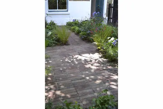 Rectilinear planted beds in front garden of white house with paths and paved areas in dark red and grey Bexhill brick paving.