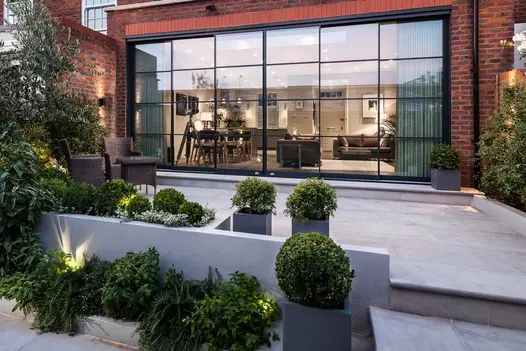 Patio with Beige sawn sandstone bullnose step up to entrance to large living room with huge glass doors. Design by EMR Architects.