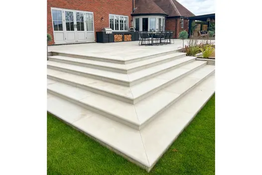 Corner of patio with 5 Beige smooth sandstone bullnose steps descending on 2 sides to lawn. Design by Ravenstone Garden Services.