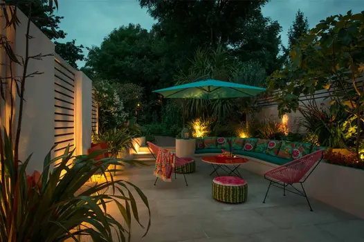 Twilight view of illuminated Beige smooth sandstone patio with round table, parasol and chairs and inbuilt bench with cushions.