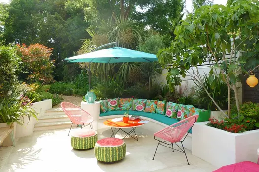 Bench seat with turquoise cushions borders Beige smooth sandstone patio with steps up to gravel path between beds.