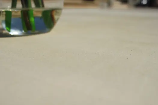 Very near close-up of Beige Smooth sandstone paving with base of glass vase in top left corner.