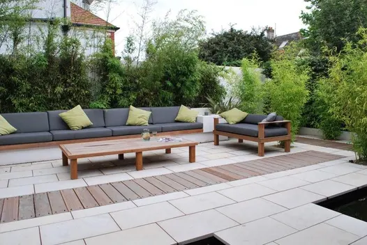 Long modular sofa sits along edge of Beige smooth sandstone patio with strip of wooden planks inset. Design by Martin Swatton.