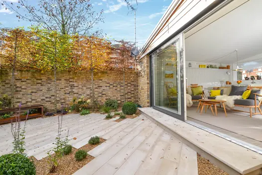 Large sliding doors of living room open onto paved area of beige smooth sandstone planks laid at angle with inset gravel beds.