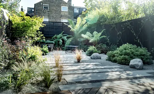 Staggered Beige Smooth sandstone plank paving with wide gravel joints laid between beds planted with grasses, low shrubs and ferns.