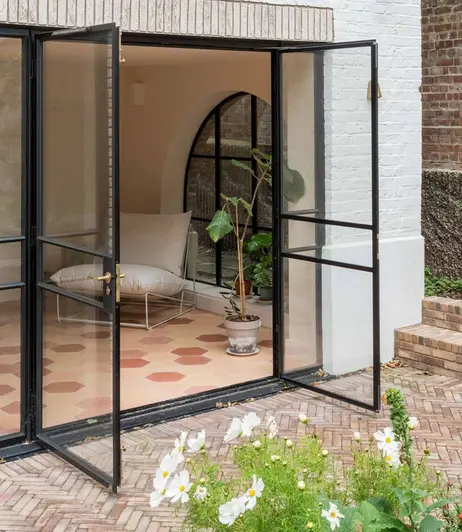 French doors of white-painted house open onto patio of Bexhill clay pavers laid in herringbone pattern, with 2 steps on right.