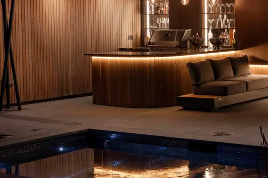 Curved bar and 3-seater sofa in illuminated interior with pond edged with Black Granite pencil round coping stones to match floor.